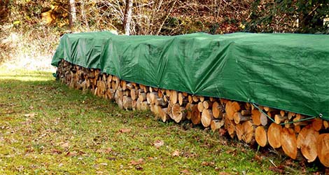 Ein grüner Schutzbezug bedeckt sorgfältig einen Holzstapel, schützt vor Nässe und Witterungseinflüssen.