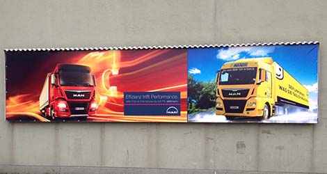 Ein Werbetransparent der Firma MAN zeigt ein LKW-Zugfahrzeug und einen Sattelauflieger von ARGE Logcom mit dem Slogan "Friend on the Road", symbolisch für Partnerschaft im Transportwesen.