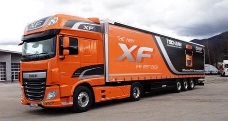 Auf dem Bild ist ein Schmitz Sattelauflieger zu sehen, dessen Schiebeplane von DAF TSCHANN digital beschriftet wurde. Die ansprechende Werbung wirbt für den neuen DAF XL Zugmaschine, der mit diesem Anhänger perfekt harmoniert.