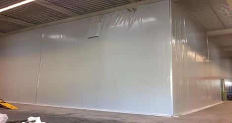 Das Bild zeigt eine Lagerhalle bei der Firma Steinbacher mit einer PVC-Planenabtrennung. Die Abtrennung ermöglicht es, Lagerbereiche effektiv zu organisieren und schützt die gelagerten Waren vor Witterungseinflüssen.