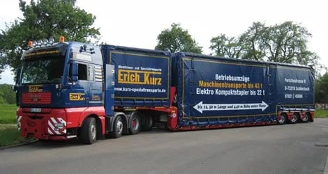 Auf dem Bild ist ein Mega Jumbo Sattelauflieger der Firma Erich Kurz zu sehen. Der Auflieger hat eine auffällige blaue Plane, auf der das Firmenbranding der Firma Erich Kurz gut sichtbar ist.